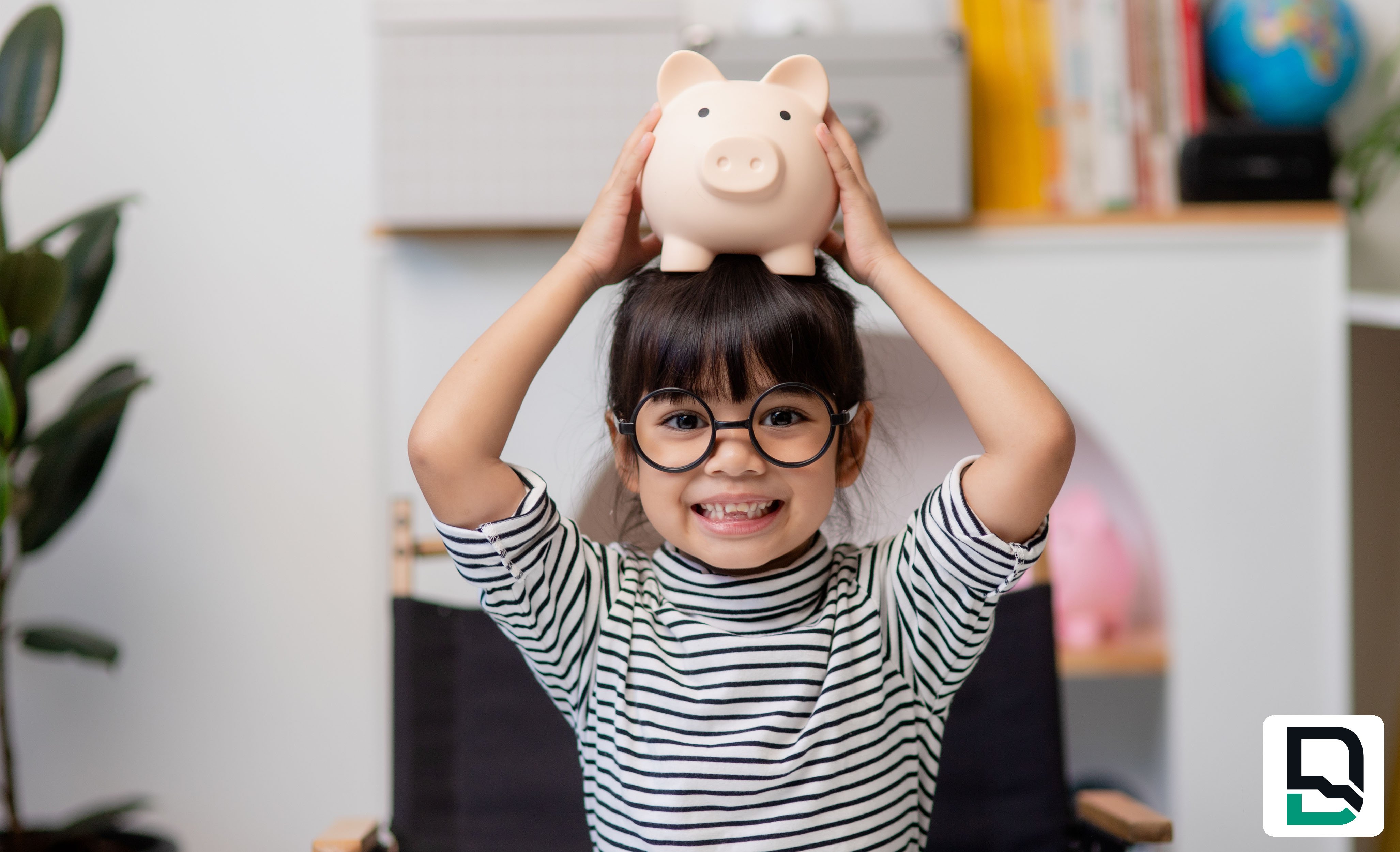Young girl wearing glasses holding piggy bank on head