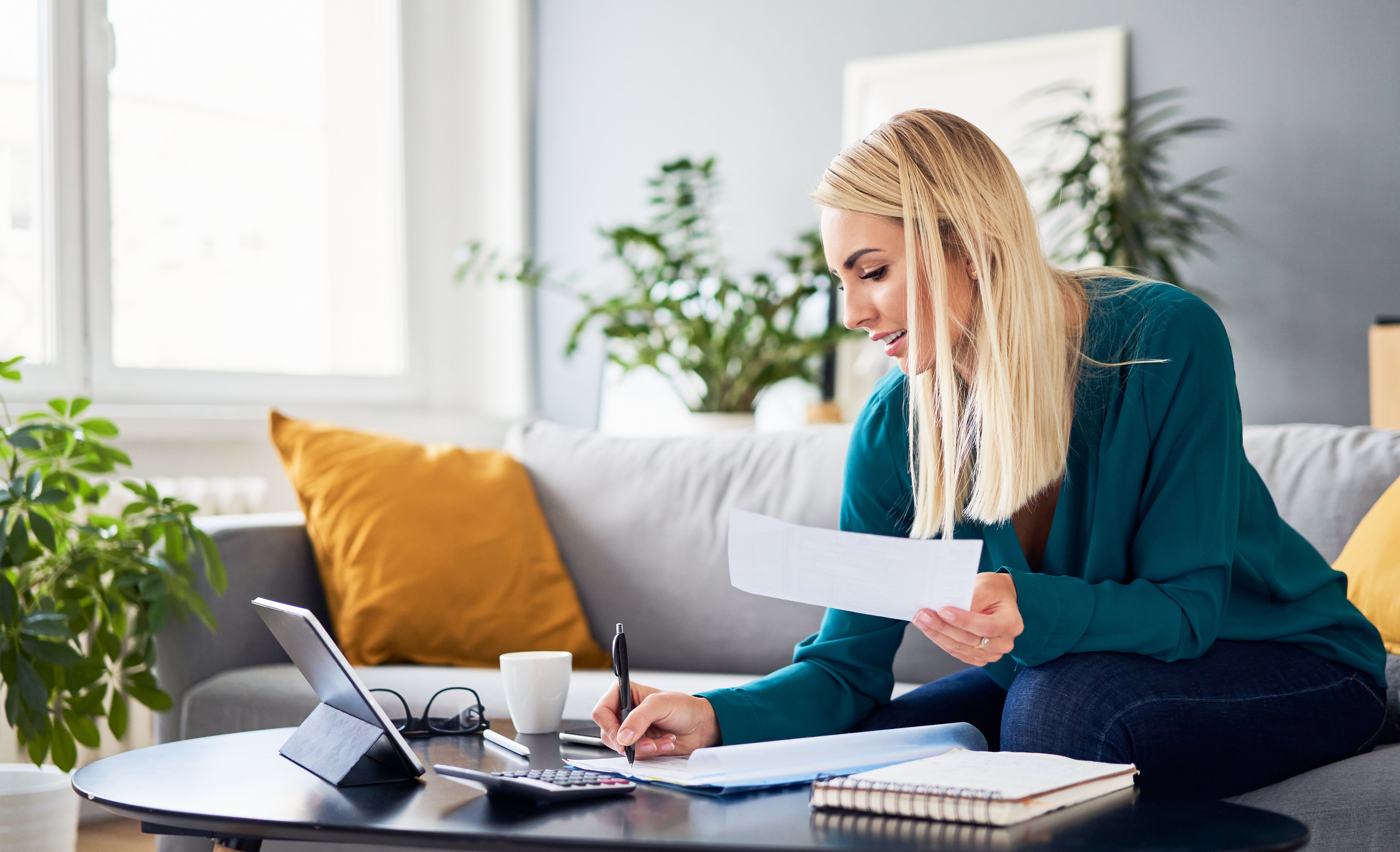 Woman sitting on couch holding bill working on laptop