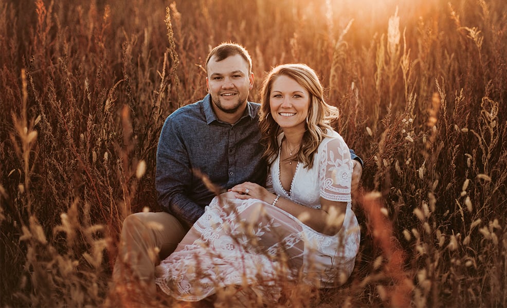 Kelbi and Austin's engagement photo sitting in field at sunset