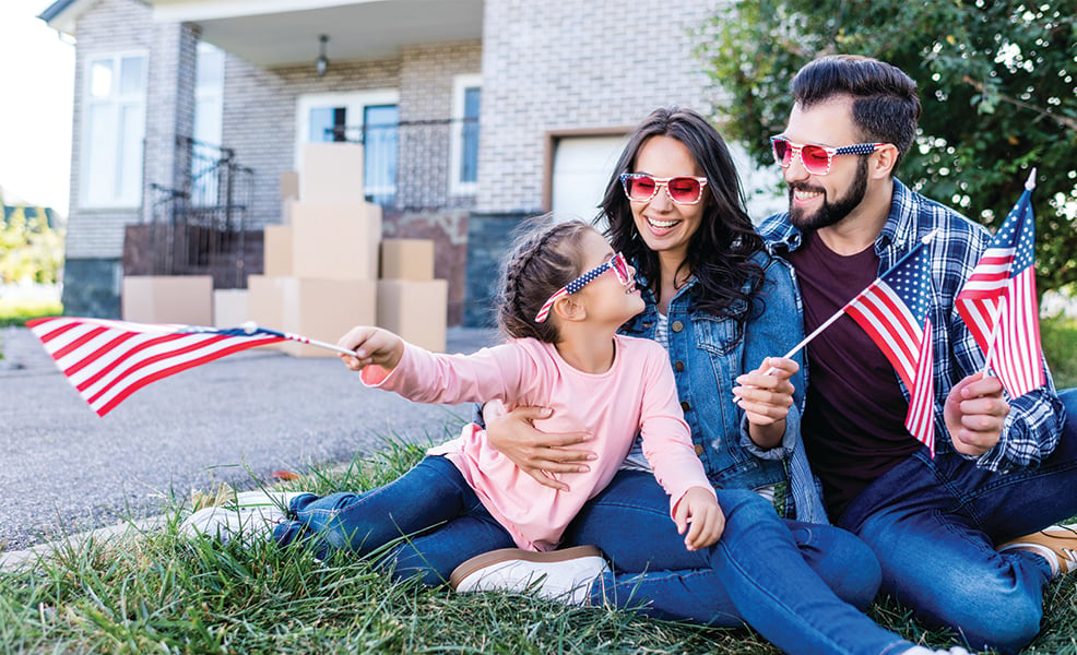 Patriotic family sitting in front of house and moving boxes