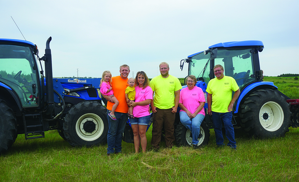 The Adolph family standing in front of two blue tractors