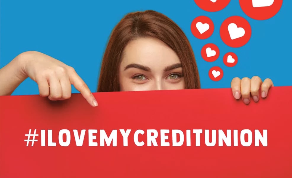 Woman with hearts over her head peaking over red sign while pointing at #ILoveMyCreditUnion