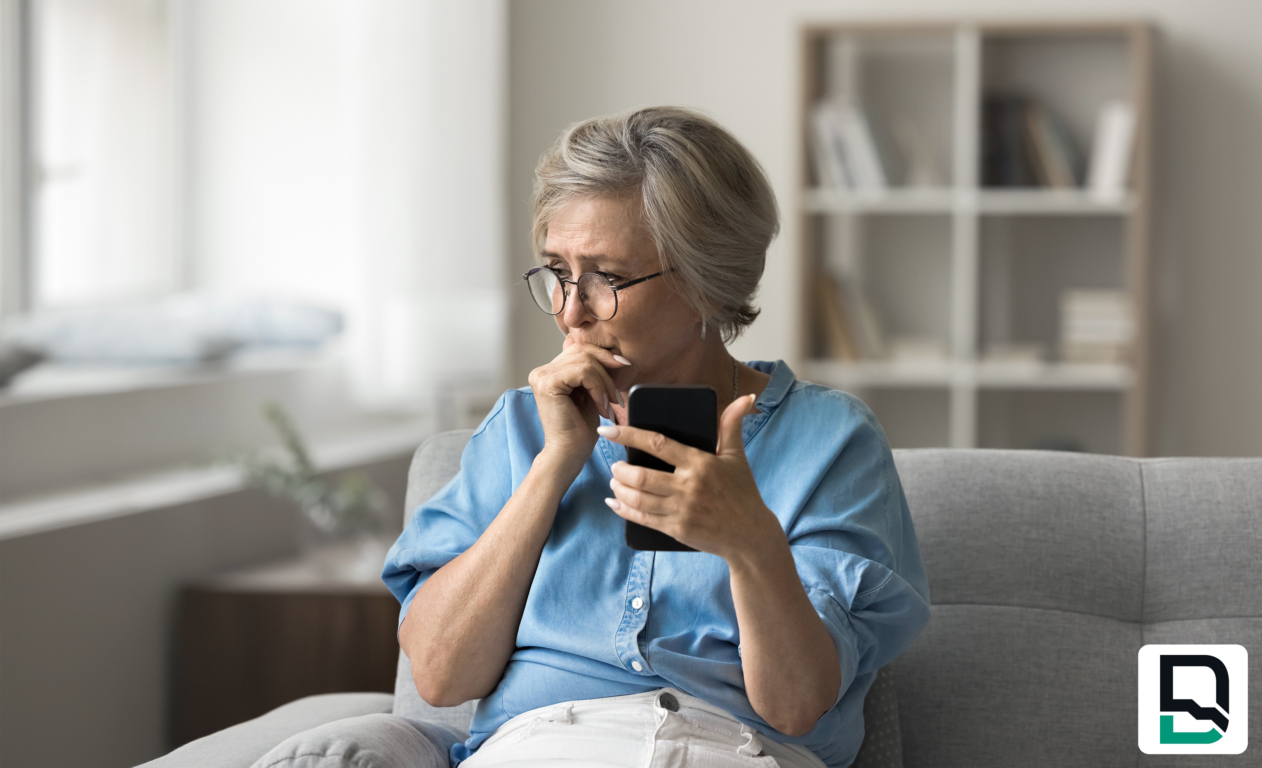 Worried elderly woman sitting on couch looking at cell phone