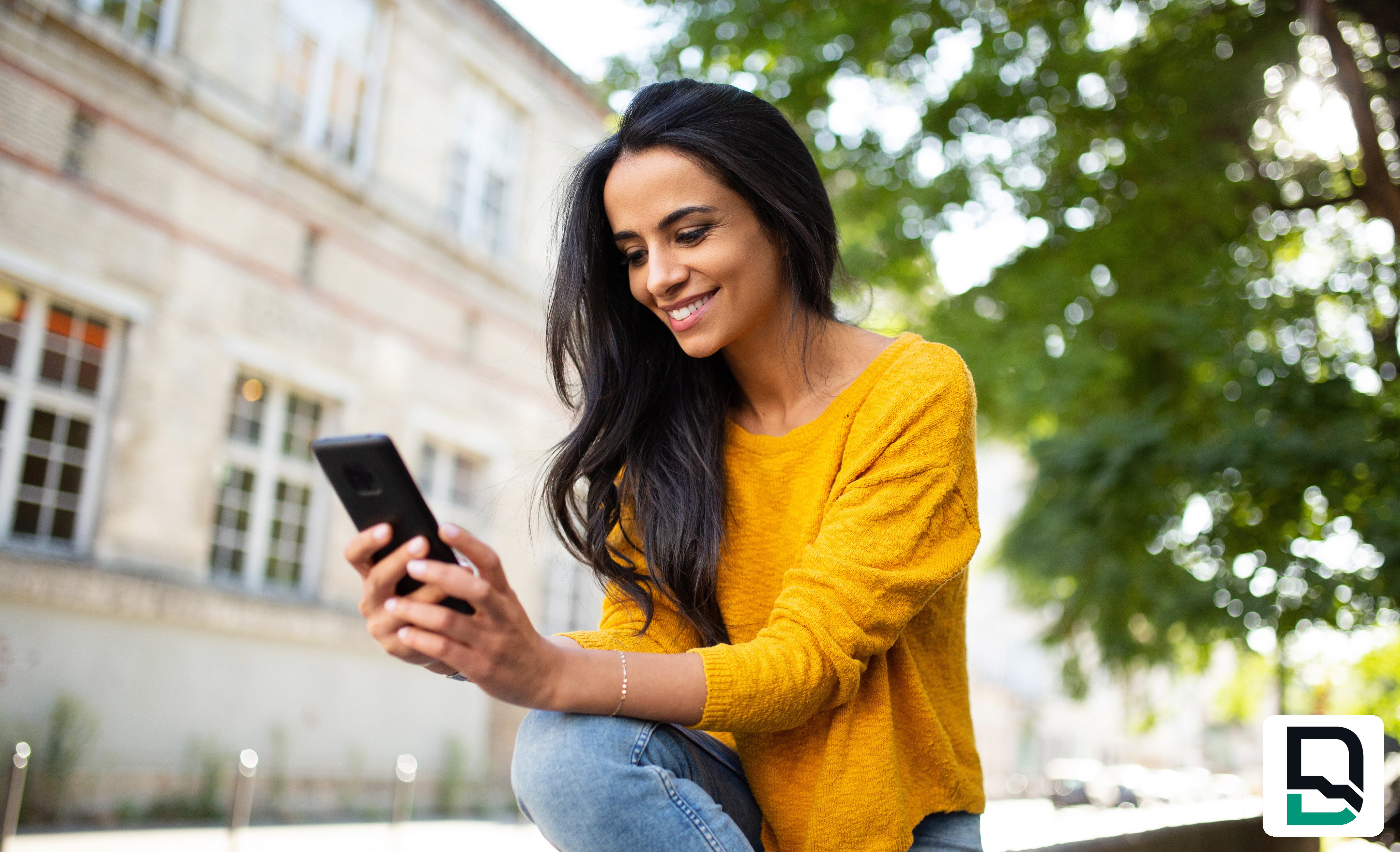 Woman wearing yellow shirt looking at phone outdoors