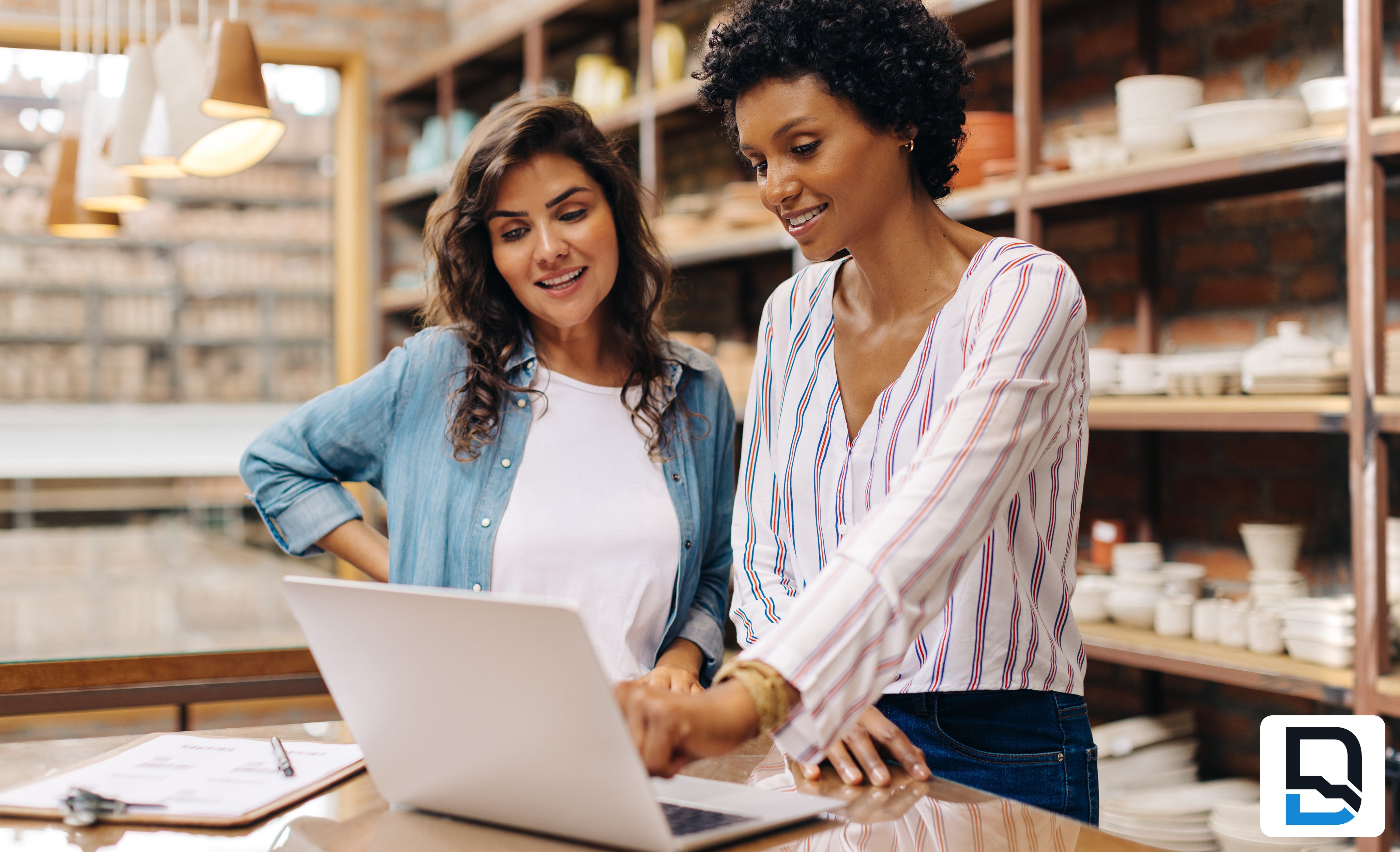 Two bi-racial women looking at laptop in ceramics store